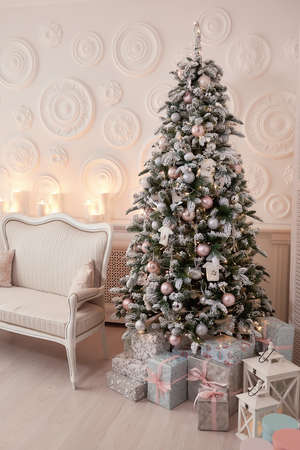 Christmas tree with a white sofa in a white room. White living room with a vintage sofa. Light Christmas tree is decorated with various toys, the gift boxes are tied with pink ribbons, vertical photoの写真素材
