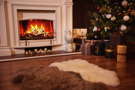 Winter holidays atmosphere in a warm room with a christmas tree full of lights and toys near a cute fireplace with fire and present toys. Christmas interior. New year designの写真素材