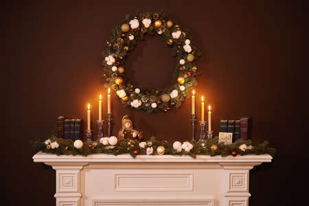 On the fireplace there are burning candles, a Christmas wreath hanging over the fireplace, Christmas decorations, brown wall in the background, books are on the fireplace, Xmas Home Interiorの写真素材