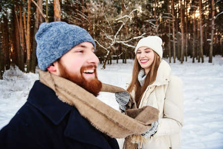 Winter fun couple playful together during winter holidays vacation outside in snow forest. A guy and a girl smiling, laughing. Weekends out of town. Xmas Morning, spending Christmas vacation together.の写真素材