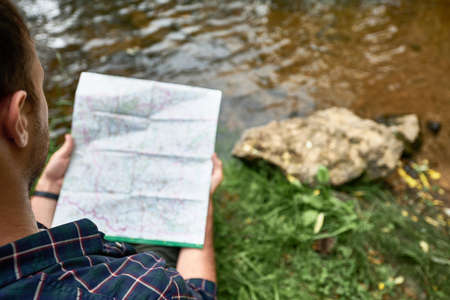Stylish hipster traveler exploring map at forest and lake in the mountains. The concept of hiking trips and traveling.New routes for recreation.Lifestyle wanderlust adventure, summer vacations outdoorsの写真素材