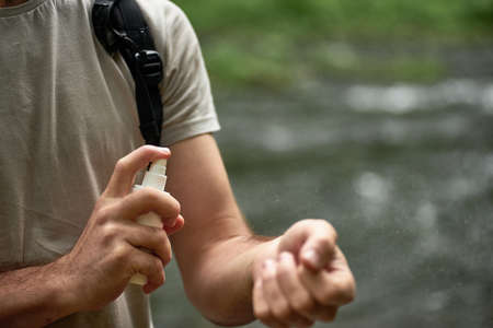 Male tourist using mosquito and tick repellent spray outdoors during hiking in forest near the river, Applying skin protection on hand, selective focusの写真素材