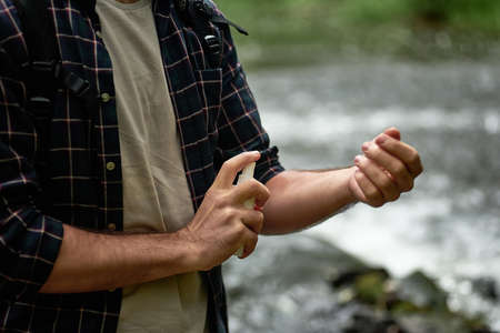 Male tourist using mosquito repellent spray outdoors during hiking in forest near the river, Applying skin protection on hand, selective focusの写真素材