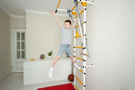 Boy doing morning fitness exercises on wall bars at home. Healthy sport and education concept. Child physical activity at home on quarantine. Sport, healhty lifestyle, active leisure at homeの写真素材