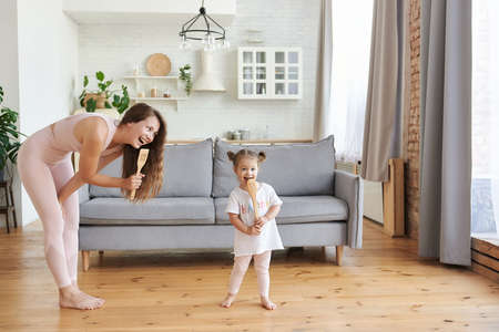 Happy young woman and her small daughter as a microphones singing songs having fun, enjoy cooking in kitchen at home turned routine into fun, food preparation everyday activity concept.の写真素材