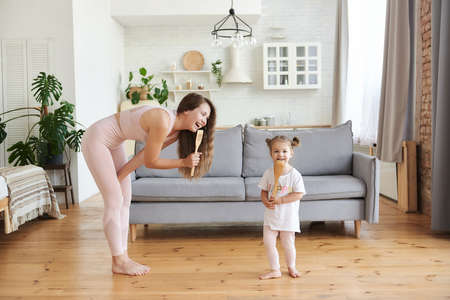 Hilarious home party. Emotional family young single mother and small daughter having fun dance listen to music at new modern kitchen. Overjoyed nanny little kid girl jump barefoot on warm wooden floorの写真素材