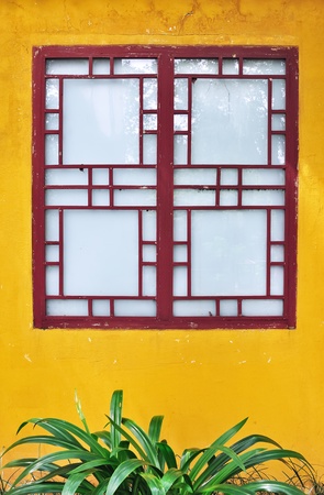 Exterior view of a traditional chinese-style wooden window set against a bright yellow painted wall ...