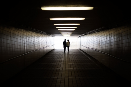 Young couple in silhouette walking towards exit of pedestrian underpassの写真素材