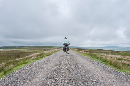 Female cyclist traveling across Northumberland moorland on the UK Coast to Coast cycle routeの写真素材
