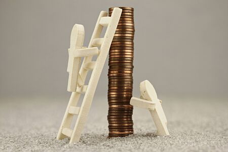 Little wooden one rises on a coin pile with a ladderの写真素材