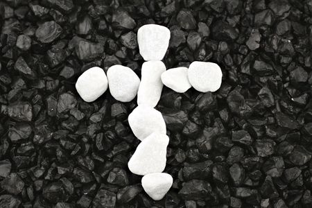 Cross of white pebbles against background of black gritの写真素材