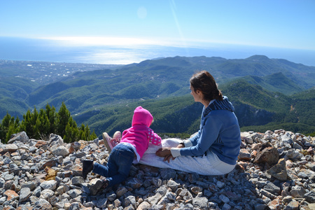 Mom and her little girl kid looking from mountains down to the seaの写真素材