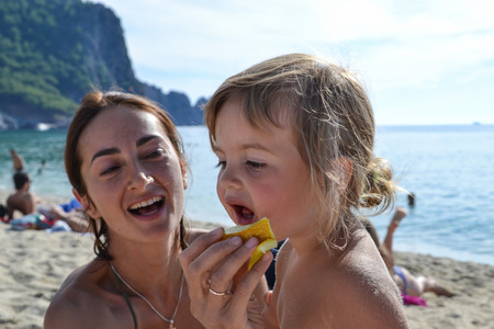 Mom feeds her little girl child with the melon on the Cleopatra beach in Alanya near the seaの写真素材