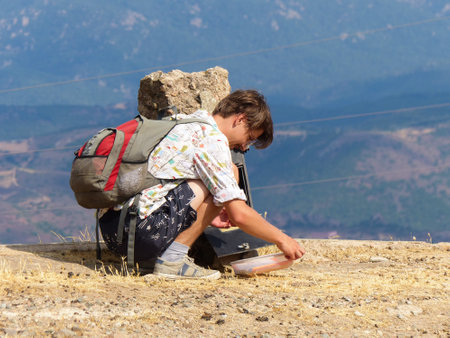 Hiker's journey on Sardinia's arid peak: On a blistering summer day, a weary hiker notes a water shortage in the summit book while kneeling on dry grass. Blurred peaks in the background highlight the intense heat.の写真素材