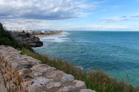 Scenic Coastal View from Faro de Cullera, Spain with Ocean Waves and Rocky Cliffside Under a Partly Cloudy Skyの写真素材