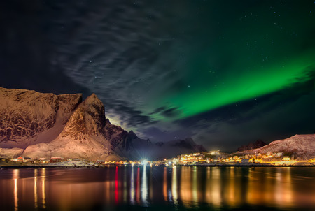 Aurora Borealis behind clouds over Reine and snowy mountains, Lofotenの写真素材