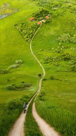 Cyclist on road toward farm amongst meadows in warp perspective, Mazury Polandの写真素材