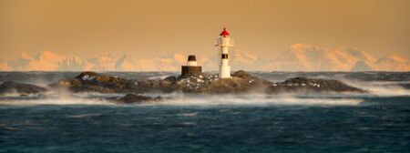 Lighthouse on little island near Vaeroya with mountains in background at sunset, Lofoten Norwayの写真素材