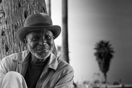 A photograph of a happy man relaxing against a tree at the beach.の写真素材