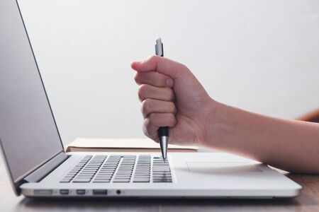 Angry woman hit laptop by pen on desk in officeの写真素材