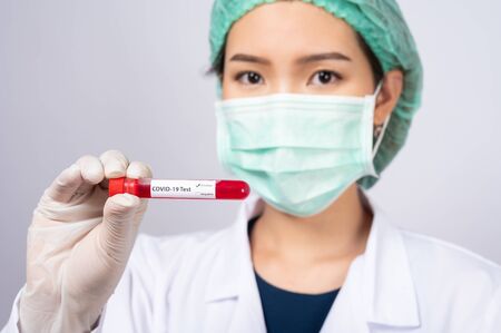Young asia doctor holding blood sample test tube on white background. concept of Coronavirus or COVID-19 outbreakの写真素材