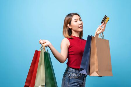 Young Asian woman in summer wear carrying shopping bags on blue background. Concept of shopping, summer sale.の写真素材