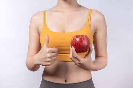A sporty Asian woman in sport wear holding fresh an apple isolated on white background. Concept of healthy lifestyleの写真素材
