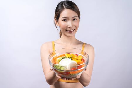 A sporty Asian woman in sportswear eating salad isolated on white background. concept of healthy lifestyle, vegetarian, wellbeingの写真素材