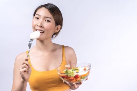 A sporty Asian woman in sportswear eating salad isolated on white background. concept of healthy lifestyle, vegetarian, wellbeingの写真素材