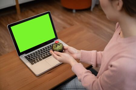 Asian woman celebrating colleague birthday through video call online virtual party at home while isolated stay at home. hand holding cup cakeの写真素材