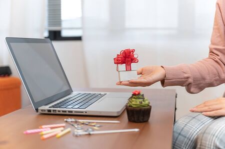Asian woman celebrating colleague birthday through video call online holding giftbox on hand while isolated stay at homeの写真素材