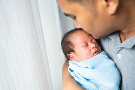 Portrait of young father kissing a newborn baby on his arm