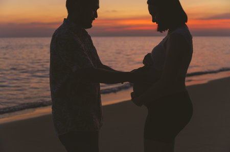 Young family and pregnant wife spend holiday on the beach at sunset