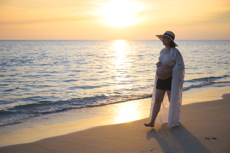 Young Asian pregnant woman relaxing walking on the beach at sunsetの写真素材
