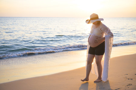 Young Asian pregnant woman relaxing walking on the beach at sunsetの写真素材