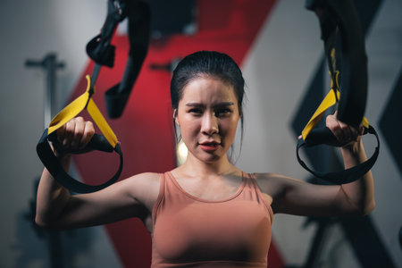 Young Asian female athlete training with trx strap hanging body for training with body resistance system in fitness gym.の写真素材