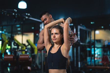Caucasian young woman in sportswear lifting dumbbell with trainer care for safety in gym.の写真素材