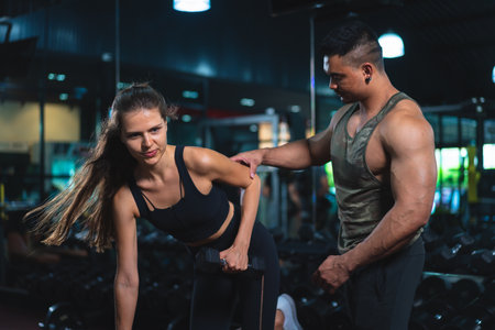 Caucasian young woman in sportswear lifting dumbbell  with trainer care for safety in fitness club or gym.の写真素材