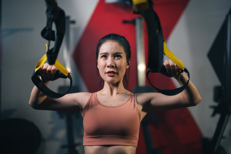 Young Asian female athlete training with trx strap hanging body for training with body resistance system in fitness gym.の写真素材
