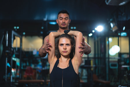 Caucasian young woman in sportswear lifting dumbbell with trainer care for safety in fitness club or gym.の写真素材