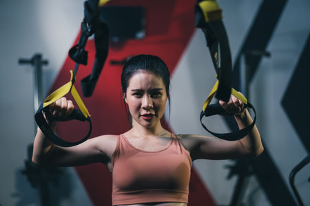 Asian female sportsperson exercising trx strap in fitness gym. Concept of bodybuilding and fitness.の写真素材