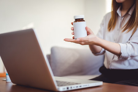 Asian female medical assistant making video call with patients for online support, Woman explaining medicine bottles working from home while coronavirus pandemicの写真素材