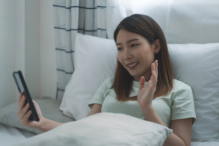 Asian woman taking selfie or making video call on smartphone to her friends or family while social distancingの写真素材