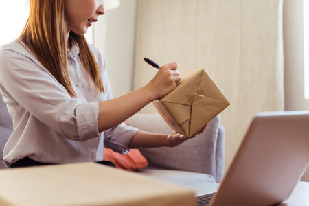 Asian woman is packing the cardboard boxes delivers to customers working from home. Female started up a small business as an online shoppingの写真素材