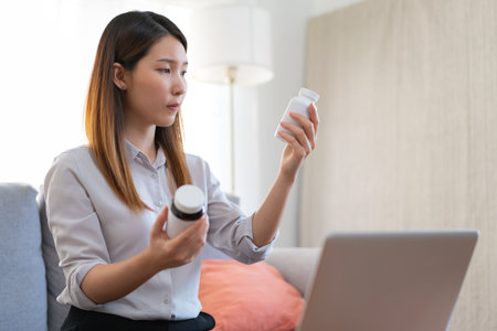 Asian female medical assistant making video call with patients for online support, Woman explaining medicine bottles working from home while coronavirus pandemicの写真素材