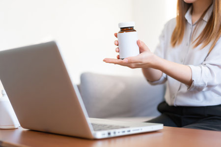 Asian female medical assistant making video call with patients for online support, Woman explaining medicine bottles working from home while coronavirus pandemicの写真素材