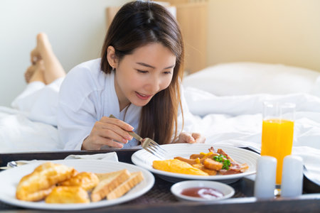 Beautiful young asian woman eating breakfast in bed in the morning.の写真素材