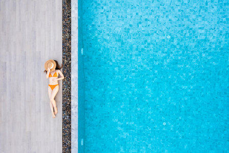 Top view of slim young woman in hat relaxing in resort swimming pool. Female enjoying sunbathing.の写真素材