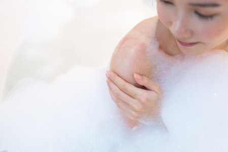 Close up relaxed woman touching skin with foam in bathtub.の写真素材