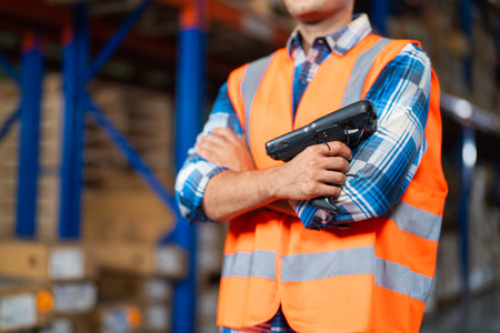 Closeup warehouse worker standing in large warehouse distribution center holding barcode reader.の写真素材